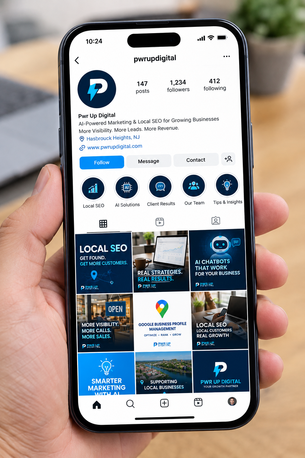 Hand holding a phone showing the Pwr Up Digital social profile with local SEO and AI marketing posts